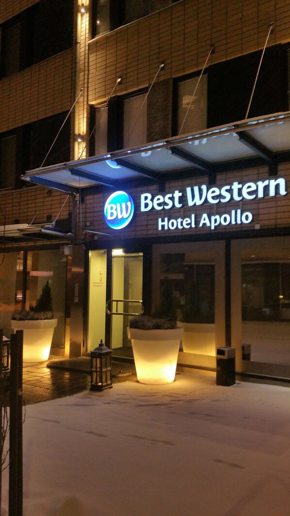 The exterior of the Best Western Hotel Apollo with a prominent illuminated sign, large potted plants, and a covered entrance area.