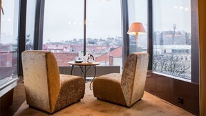 A room with two armchairs, a small table, and a lamp. Large windows offer a view of buildings and trees. - Best Western Santakos Hotel (Kaunas)