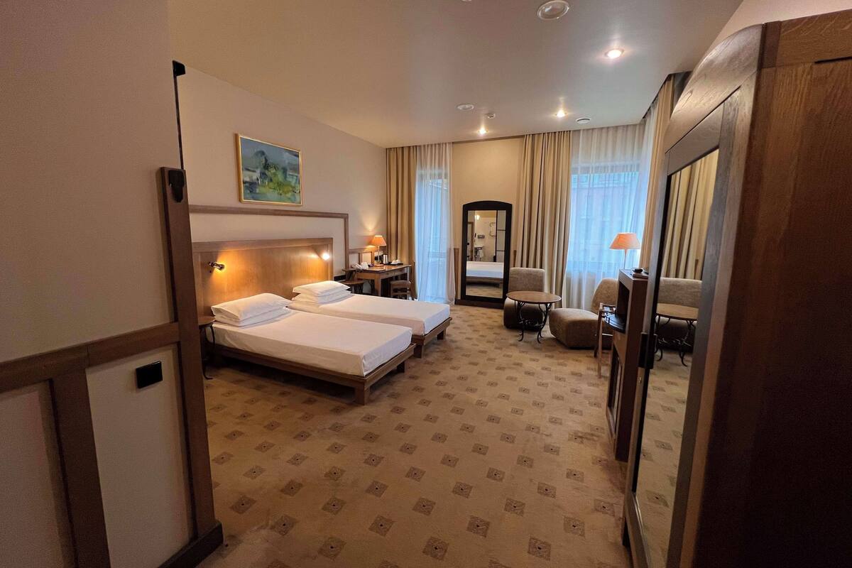 A hotel room with two beds, a desk, a chair, a mirror, and a carpeted floor.