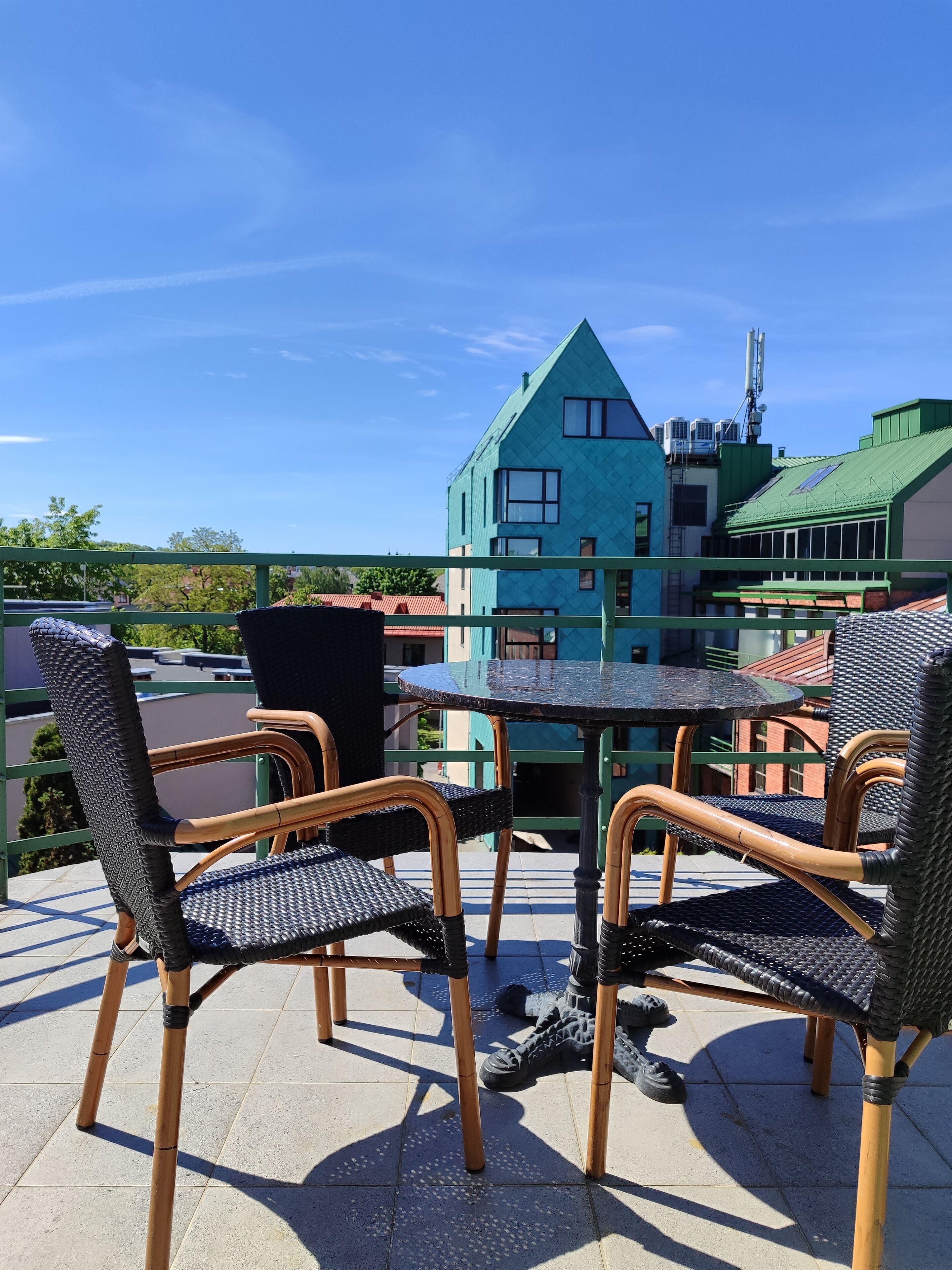 An outdoor seating area with wicker chairs and a table, overlooking a building with a green roof and multiple windows.