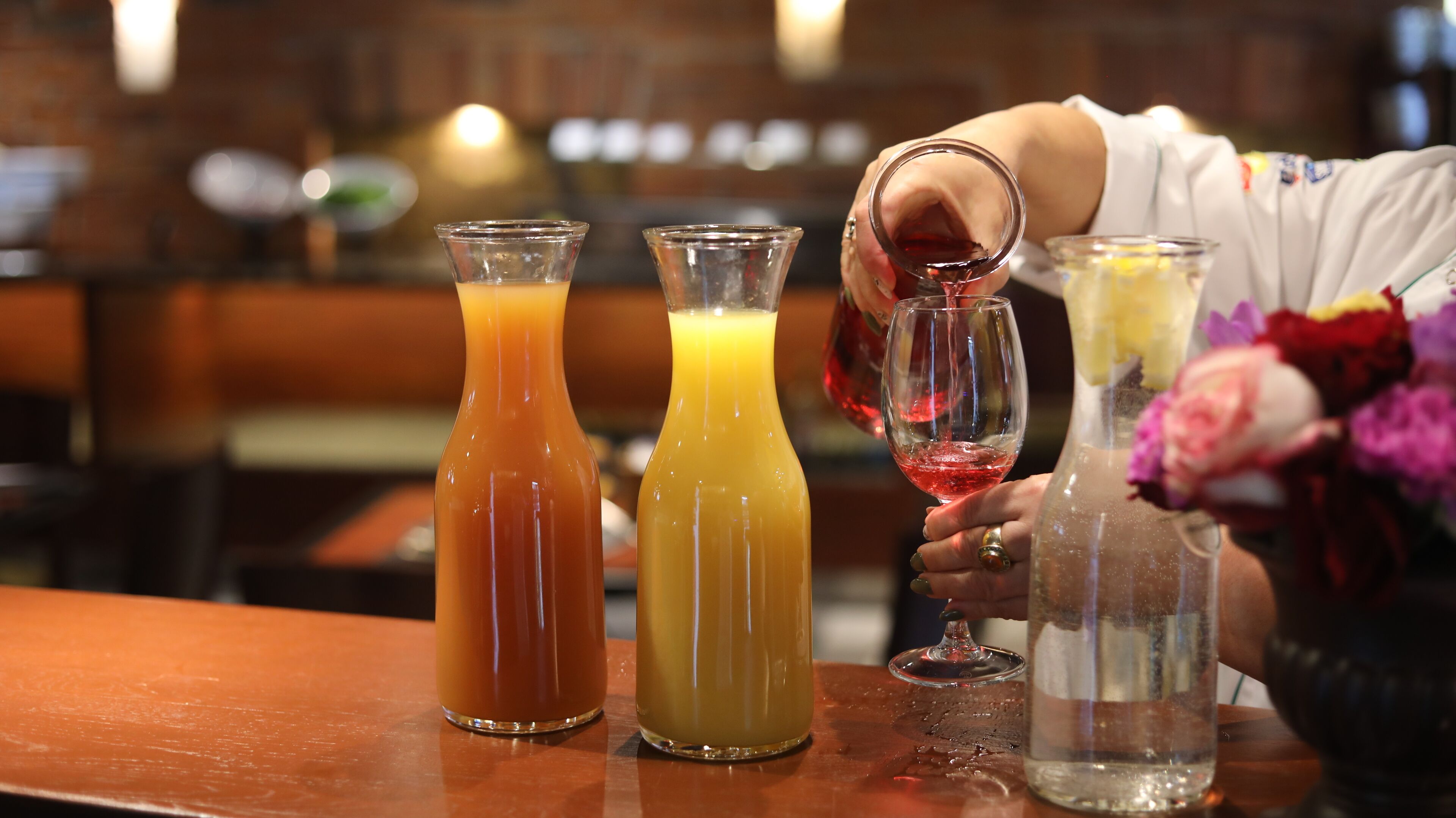 A bar setting with three bottles of different colored beverages and a hand pouring a red drink into a glass.