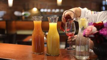 A bar setting with three bottles of different colored beverages and a hand pouring a red drink into a glass.