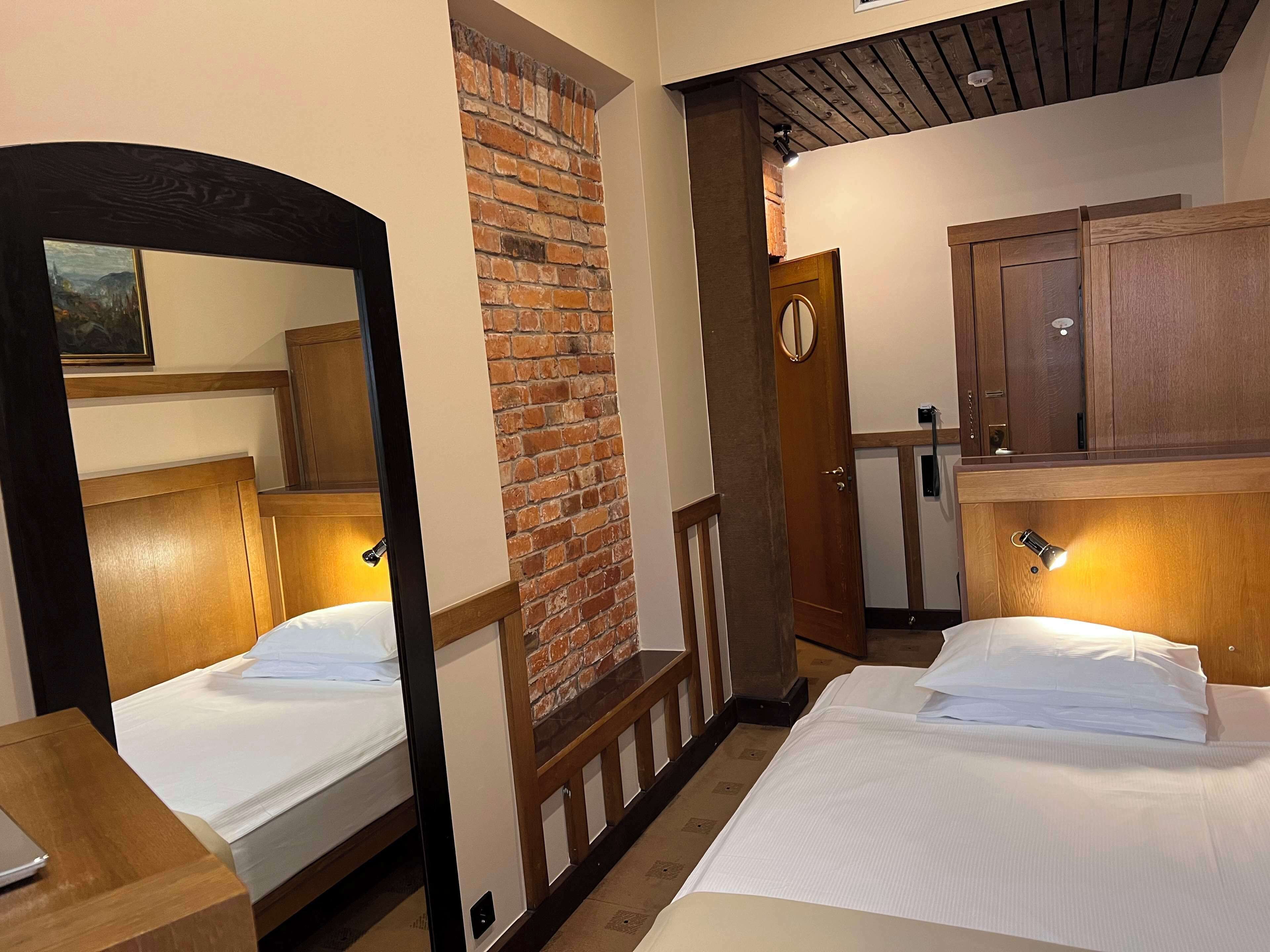 Habitación de hotel con dos camas, pared de ladrillo, cabeceros de madera y un espejo.
