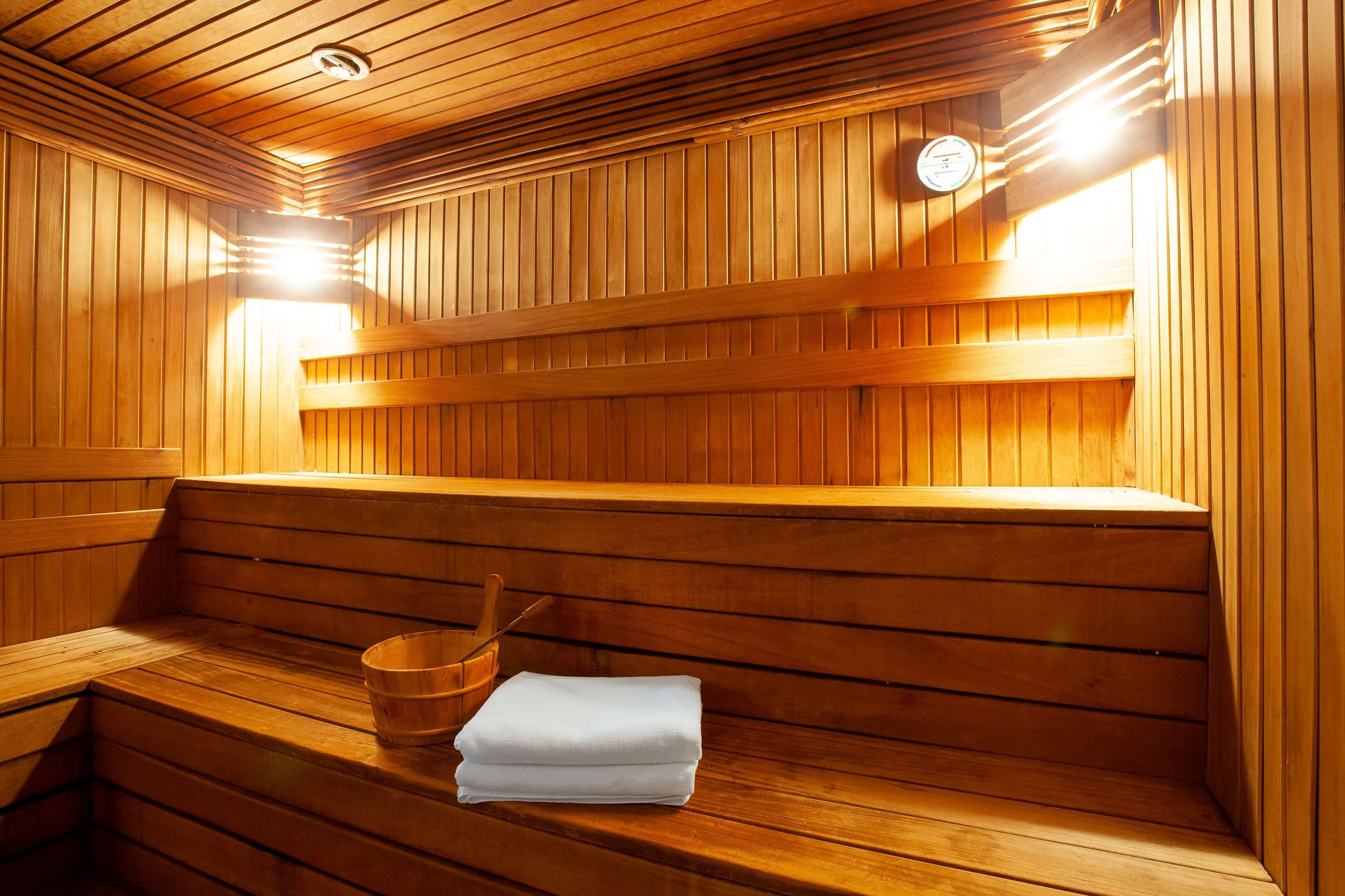 A sauna with wooden benches, a bucket, and towels.