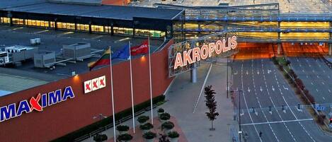 Un grand bâtiment portant l’enseigne « MAXIMA » et un panneau « AKROPOLIS ».
