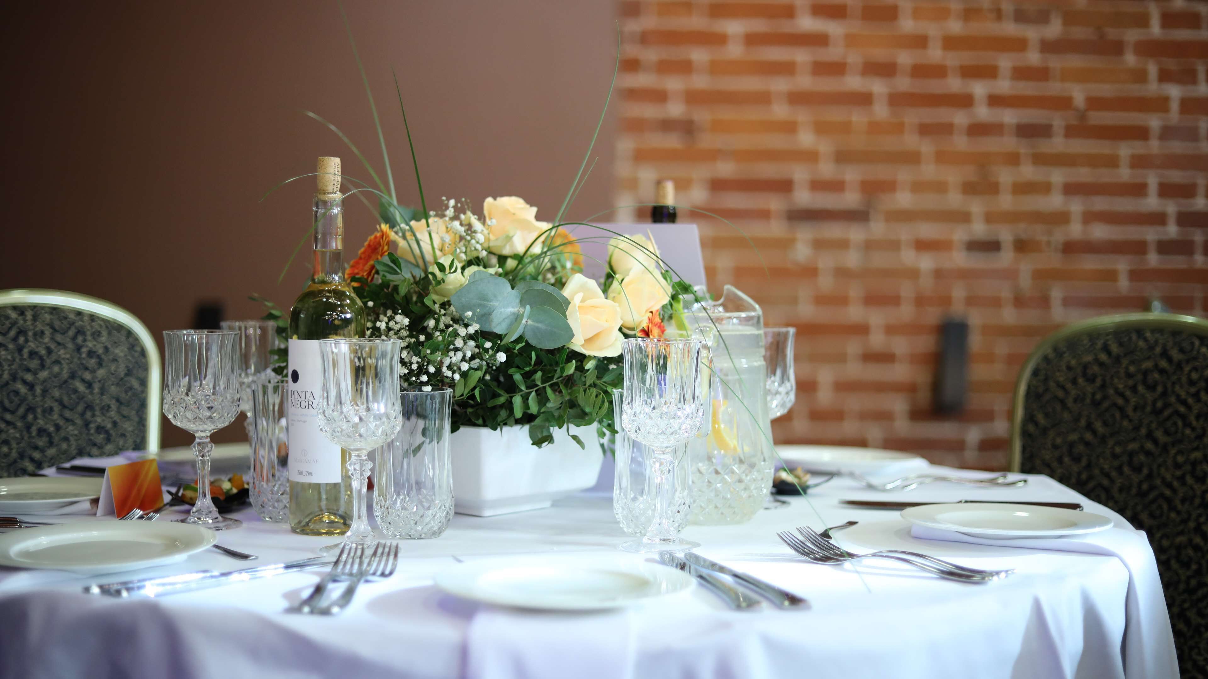 A table set for a formal dining event with a floral centerpiece, clear glassware, and a bottle of wine.