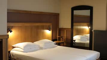 A hotel room with a wooden headboard, two bedside lamps, a round wooden table, and a large mirror.