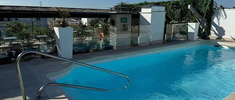A swimming pool with a metal ladder, lounge chairs, and tables.