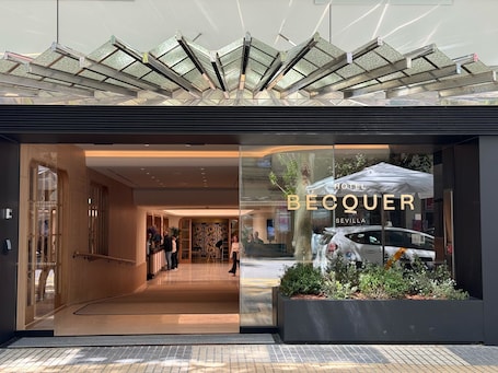 A hotel entrance with a modern design, featuring a glass facade and a visible car parked outside.