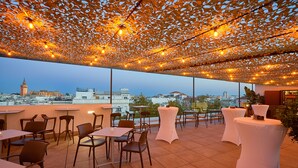 An outdoor dining area with tables and chairs, a view of a cityscape, and string lights. - Becquer Hotel, Historic City Center (Seville)