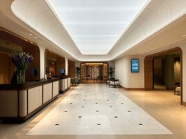 A hotel lobby with a reception desk, seating area, and a patterned wall in the background.