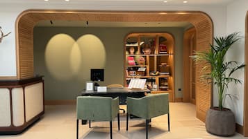 Un espacio de oficina moderno con un mostrador de recepción de madera, una computadora, dos sillas y una estantería llena de libros y objetos decorativos.