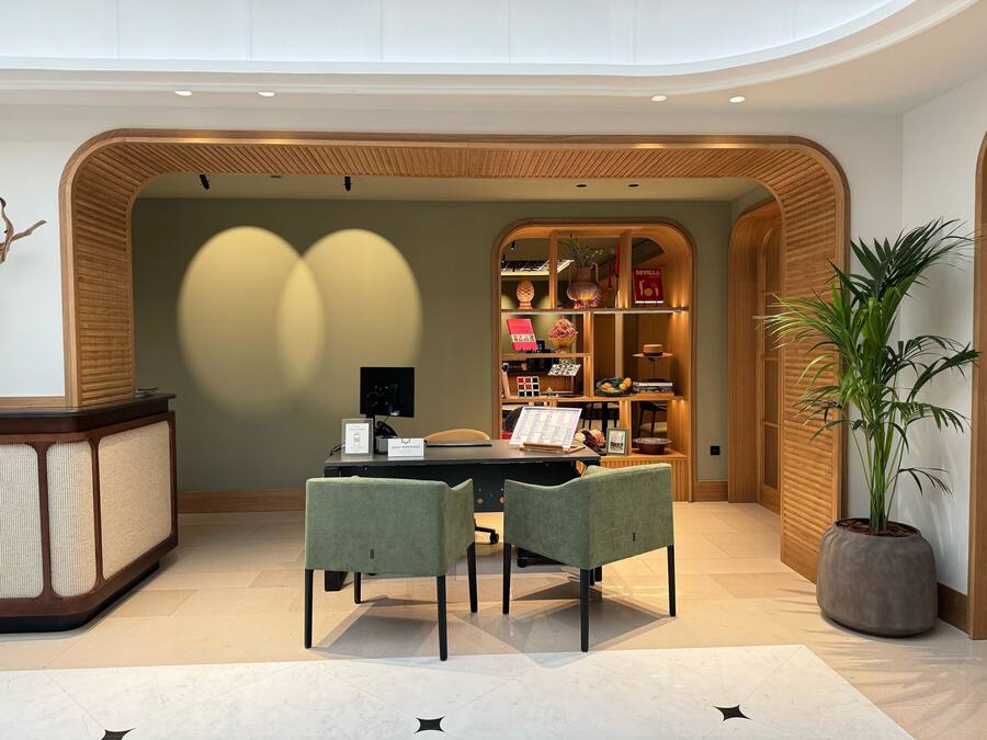 A modern office space with a wooden reception desk, a computer, two chairs, and a bookshelf filled with books and decorative items.