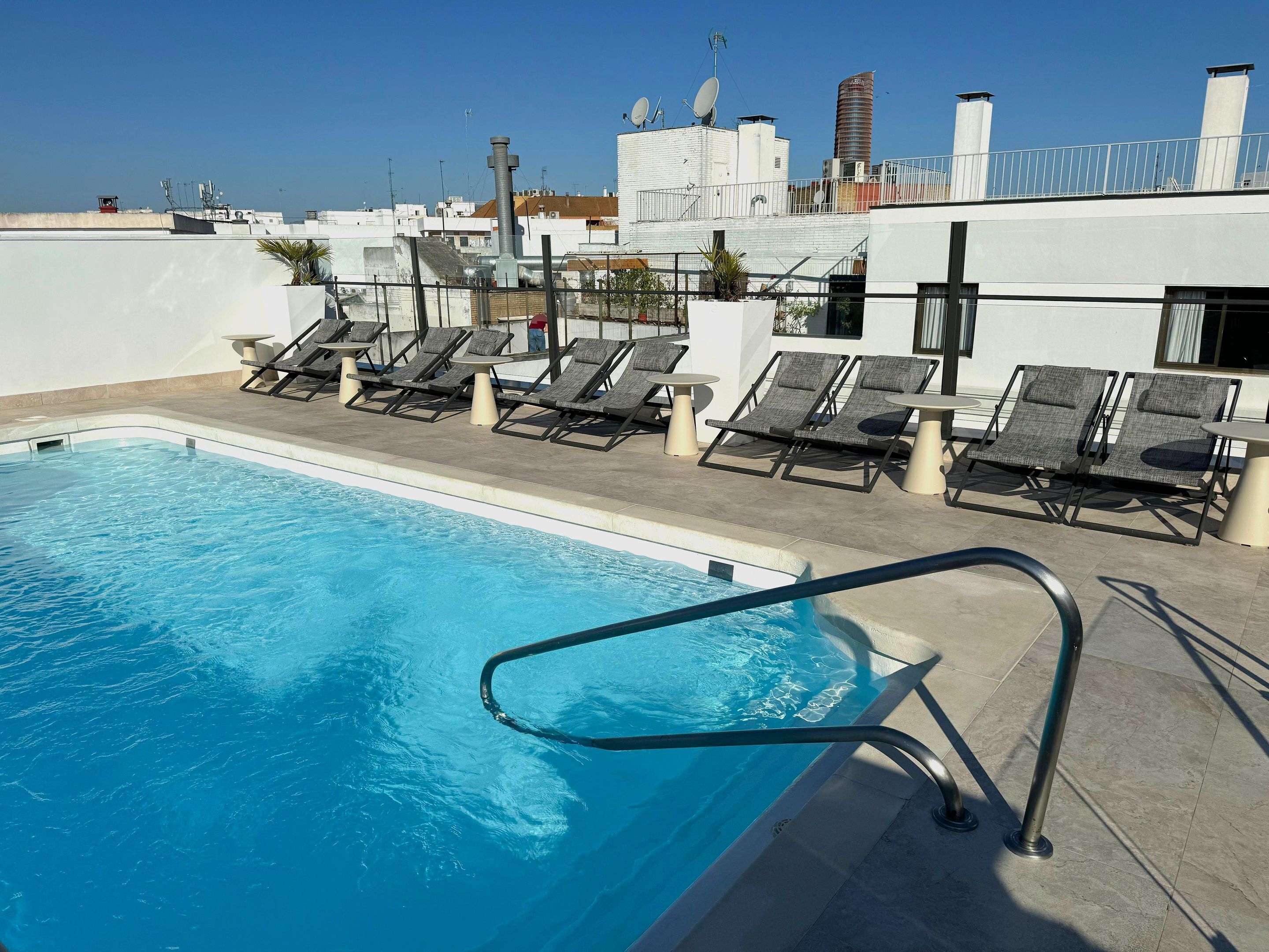 Una piscina en la azotea con sillones de descanso y vistas panorámicas de la ciudad.