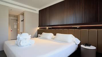 A hotel room with a large bed, a headboard with vertical lines, a bedside table with a phone, and a wall-mounted light.