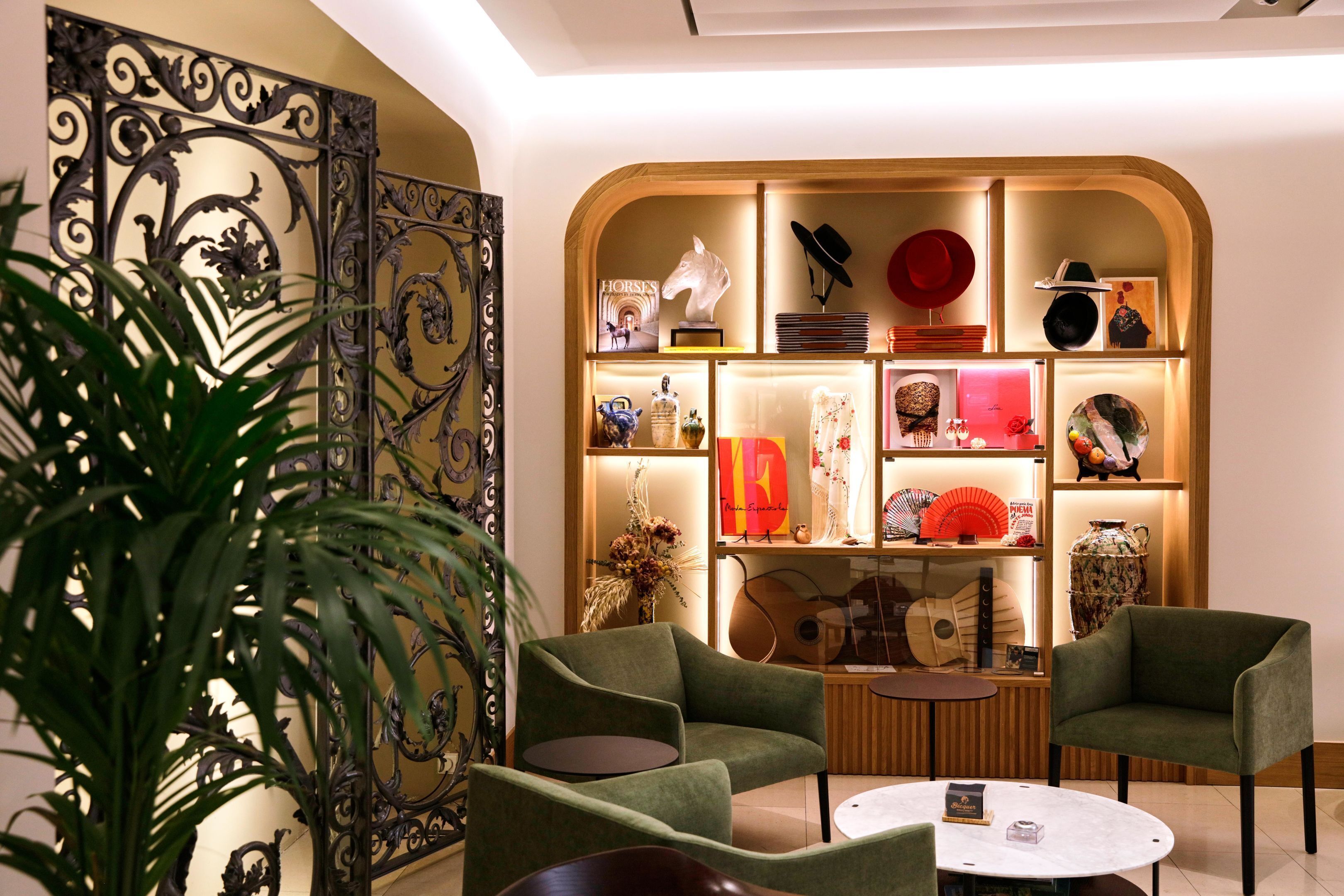 A modern interior with two green armchairs, a round table, and a decorative wall with various items.