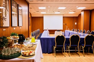 A conference room with a long table set for a meeting, equipped with chairs, a projector screen, and a buffet with various food items.