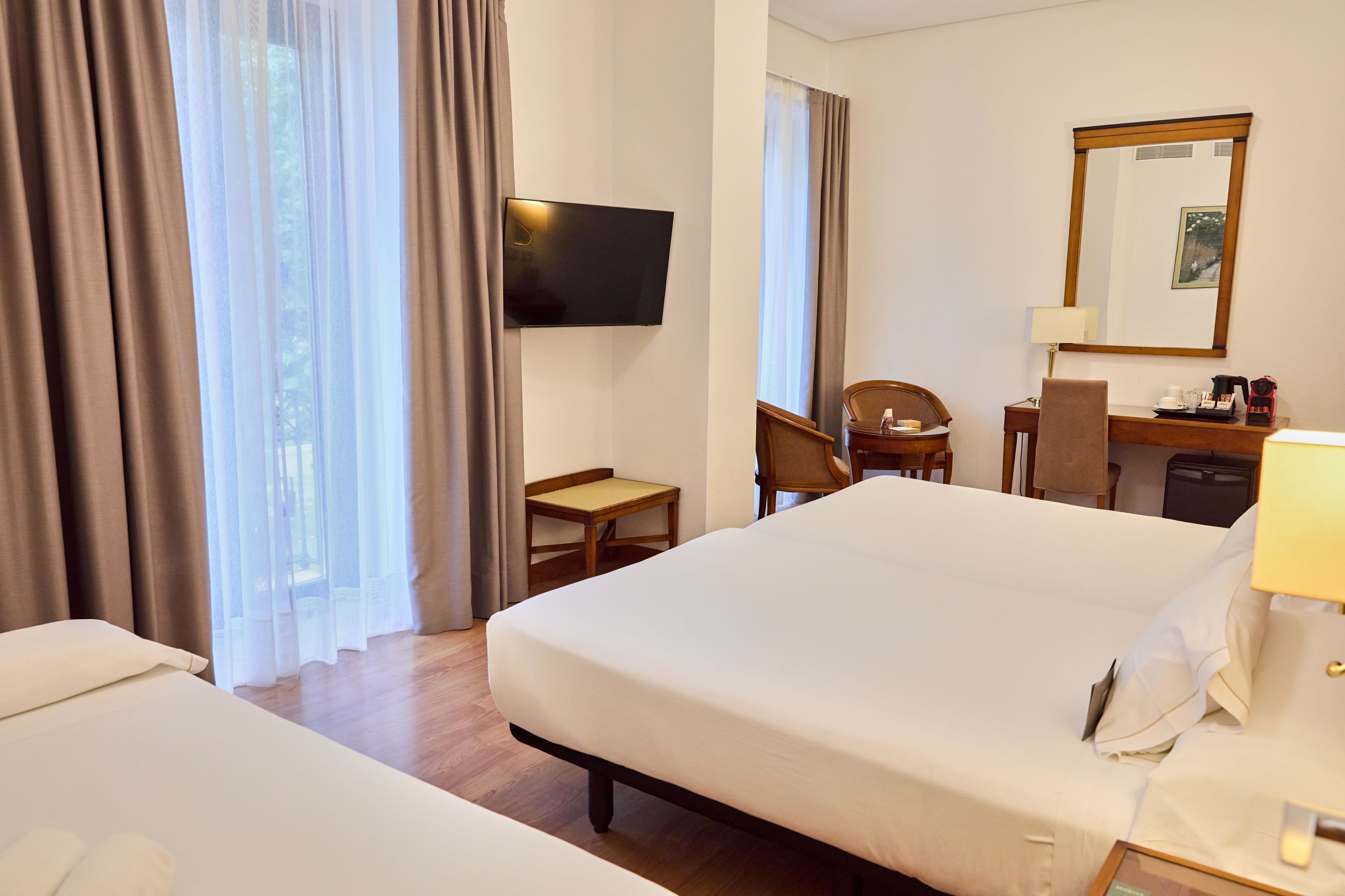 A hotel room with a bed, a desk, a chair, a television, and a mirror.