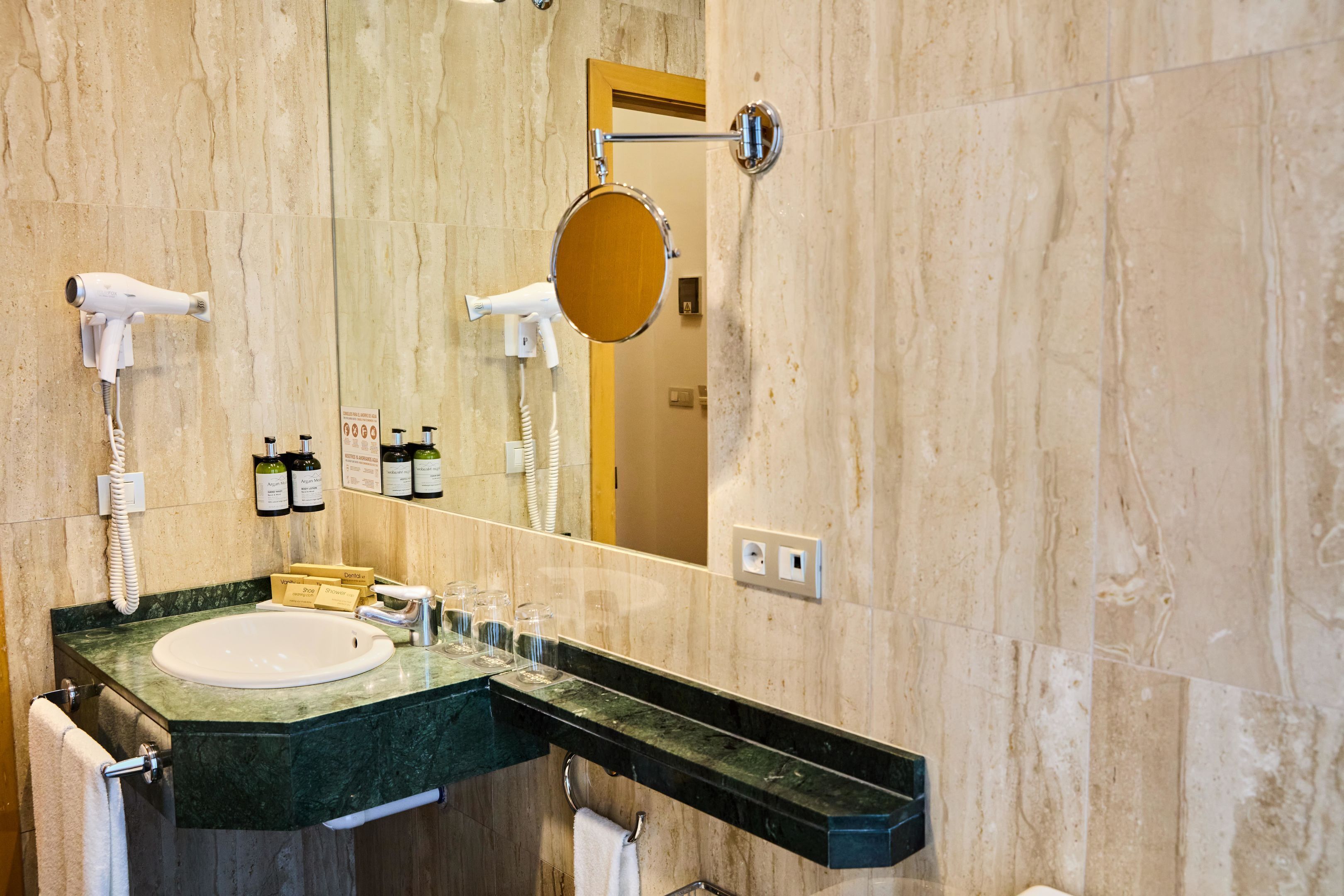 A bathroom with a sink, mirror, hairdryer, and towel rack.