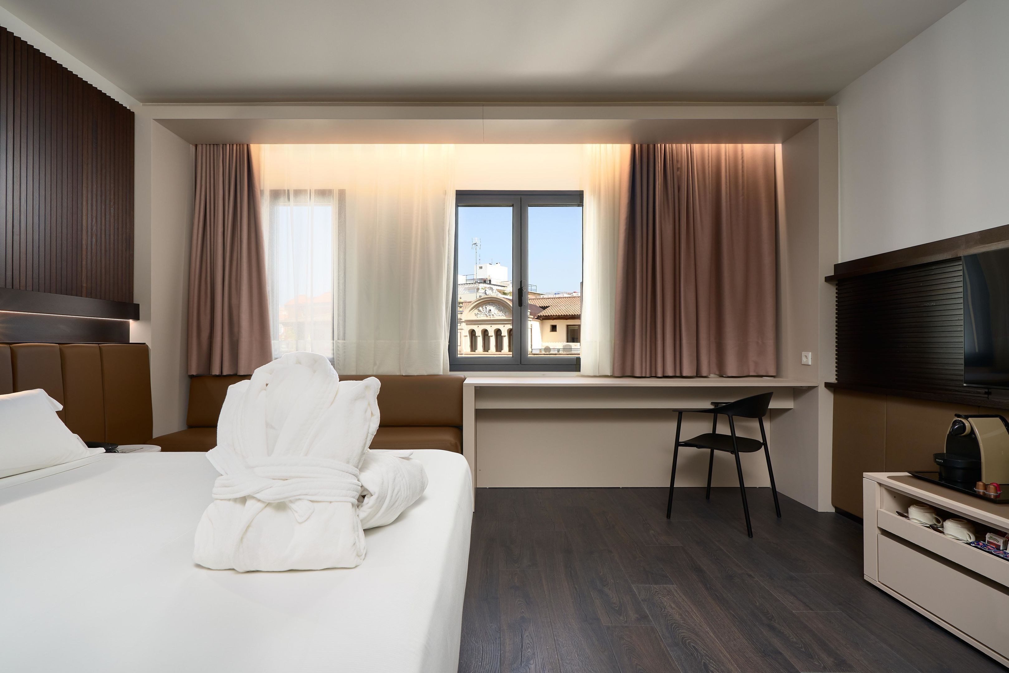 A hotel room with a bed, a desk, a chair, a TV, and a window with curtains.