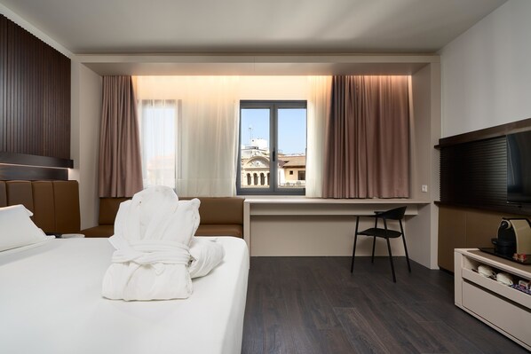 A hotel room with a bed, a desk, a chair, a TV, and a window with curtains.