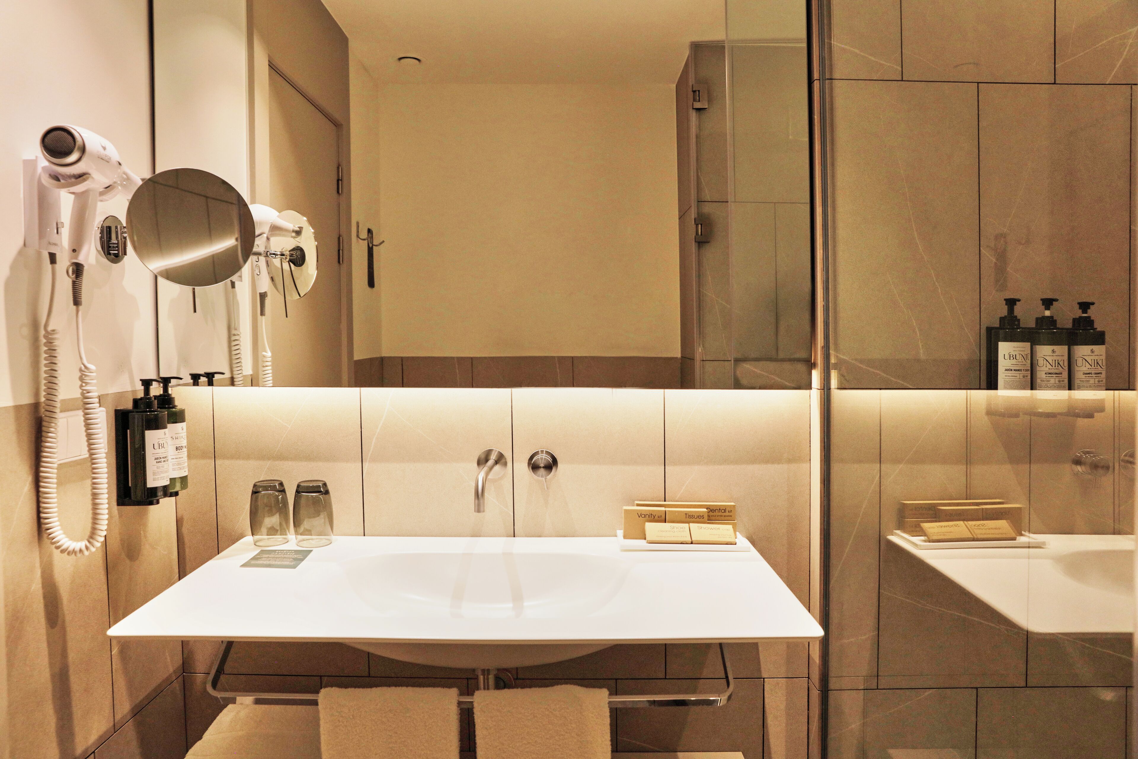 Een moderne badkamer met een grote spiegel, een haardroger en toiletartikelen.