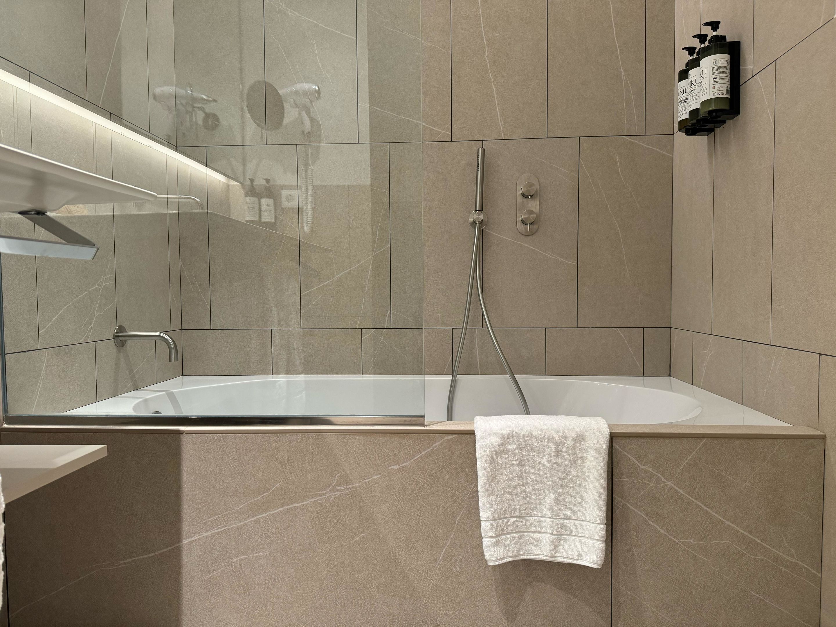 A modern bathroom with a large bathtub, a handheld showerhead, and a towel hanging on the wall.