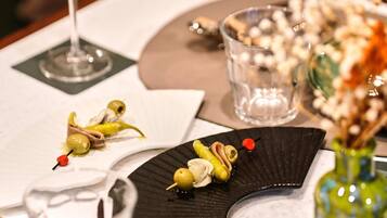 A dining table with a glass of white wine, a small glass, and a decorative plate with olives and a cherry.