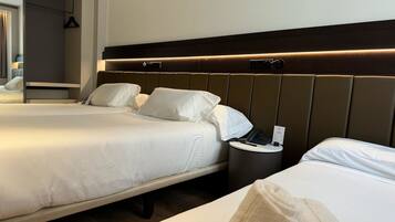A hotel room with two beds, a bedside table with a phone and a sign, and a mirror.