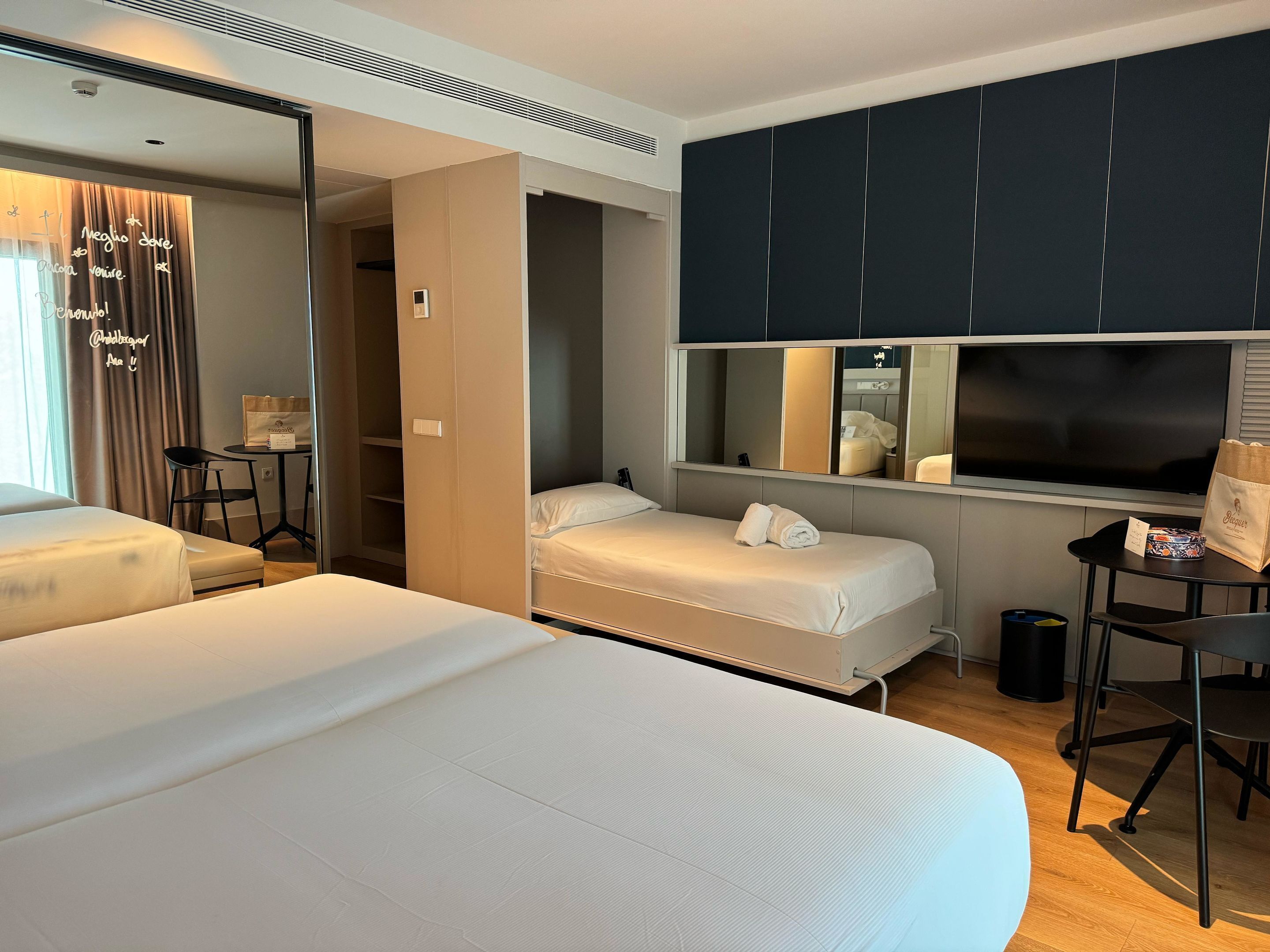 Une chambre d’hôtel avec deux lits, un bureau, une chaise, un miroir et un téléviseur.
