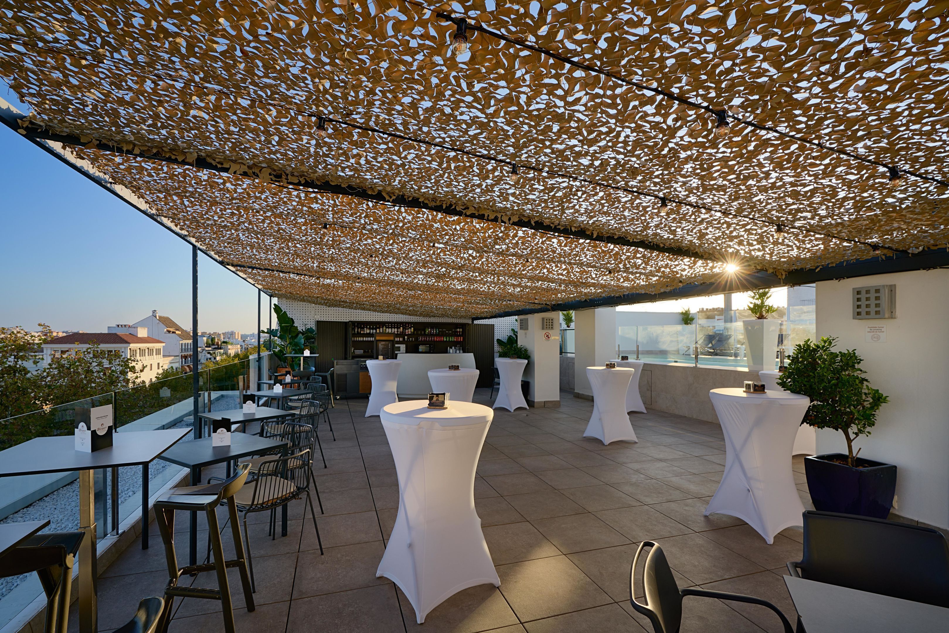 An outdoor terrace with tables and chairs, a bar area, and a view of the cityscape.