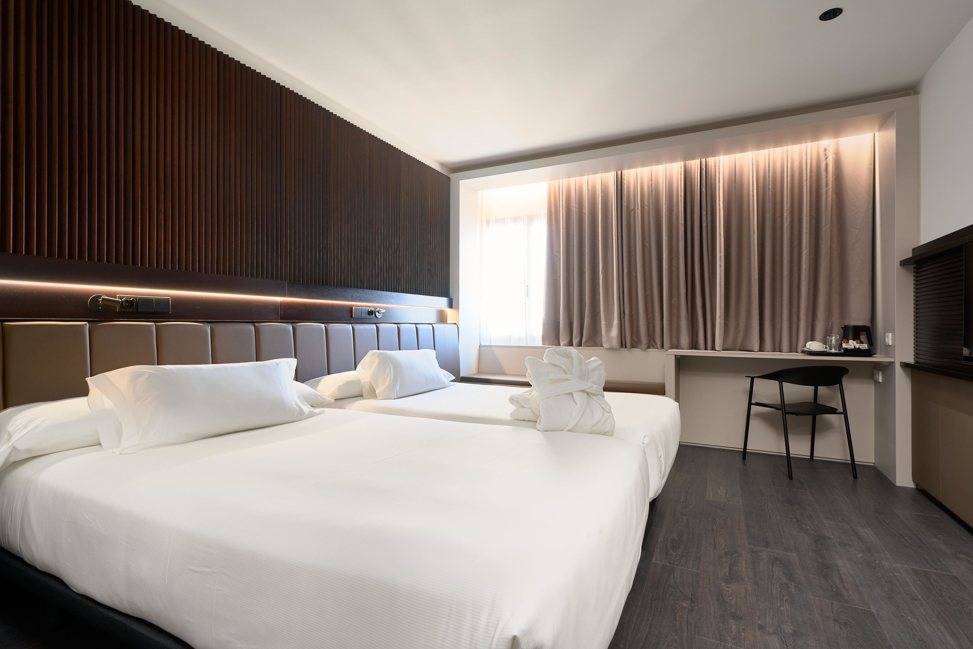 A hotel room with two beds, a desk, and a chair.