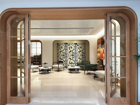 A modern interior with a wooden-framed entrance, a patterned wall, and a seating area with round tables and chairs.