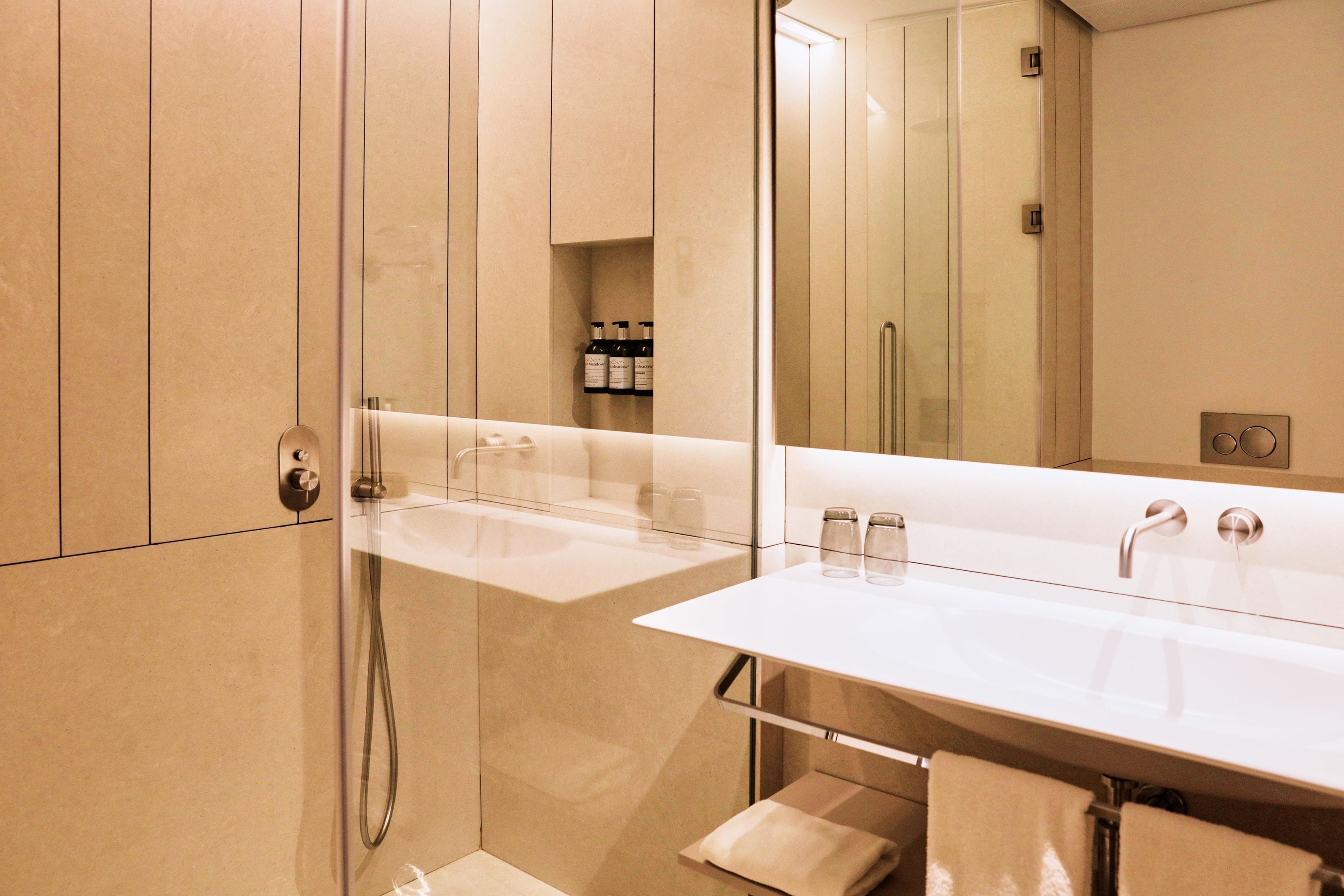 Un baño moderno con ducha de vidrio, lavamanos blanco y un espejo grande.