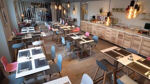 Un comedor moderno con varias mesas y sillas, una encimera de cocina con alimentos y lámparas colgantes.