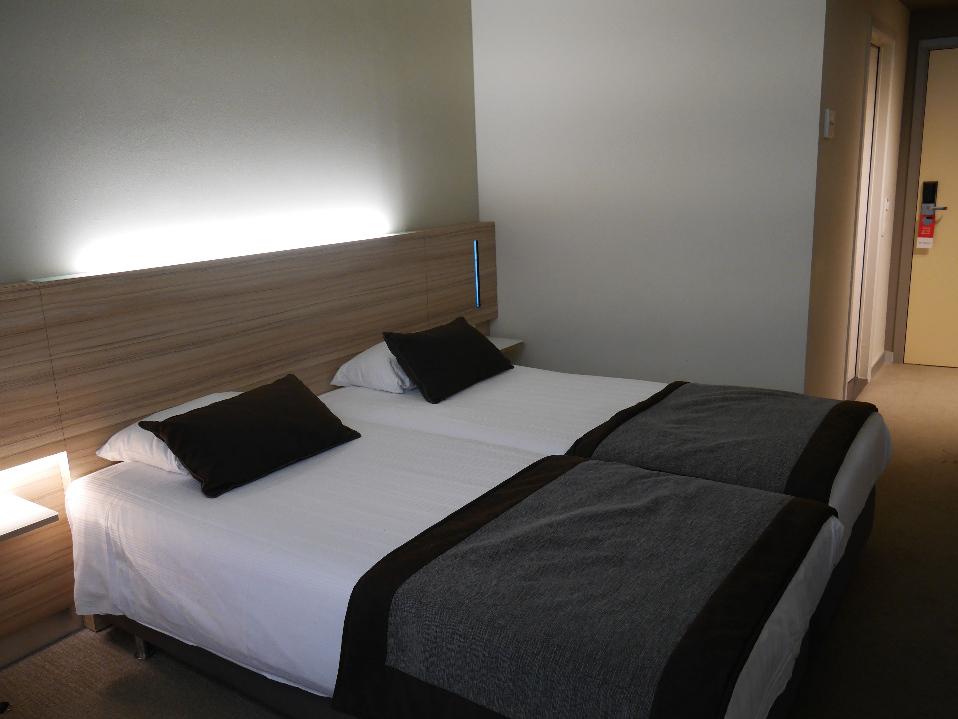 A double bed with a wooden headboard, two black pillows, and a grey blanket.