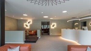 Un hall d’hôtel moderne avec des sièges en cuir, un comptoir d’accueil et un plafond au design géométrique.