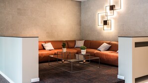 Un salon moderne avec un canapé d’angle, une table basse en verre et un luminaire au design géométrique fixé au mur.