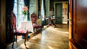 Een kamer met houten vloeren, een tafel met een bloevas en twee versierde stoelen.