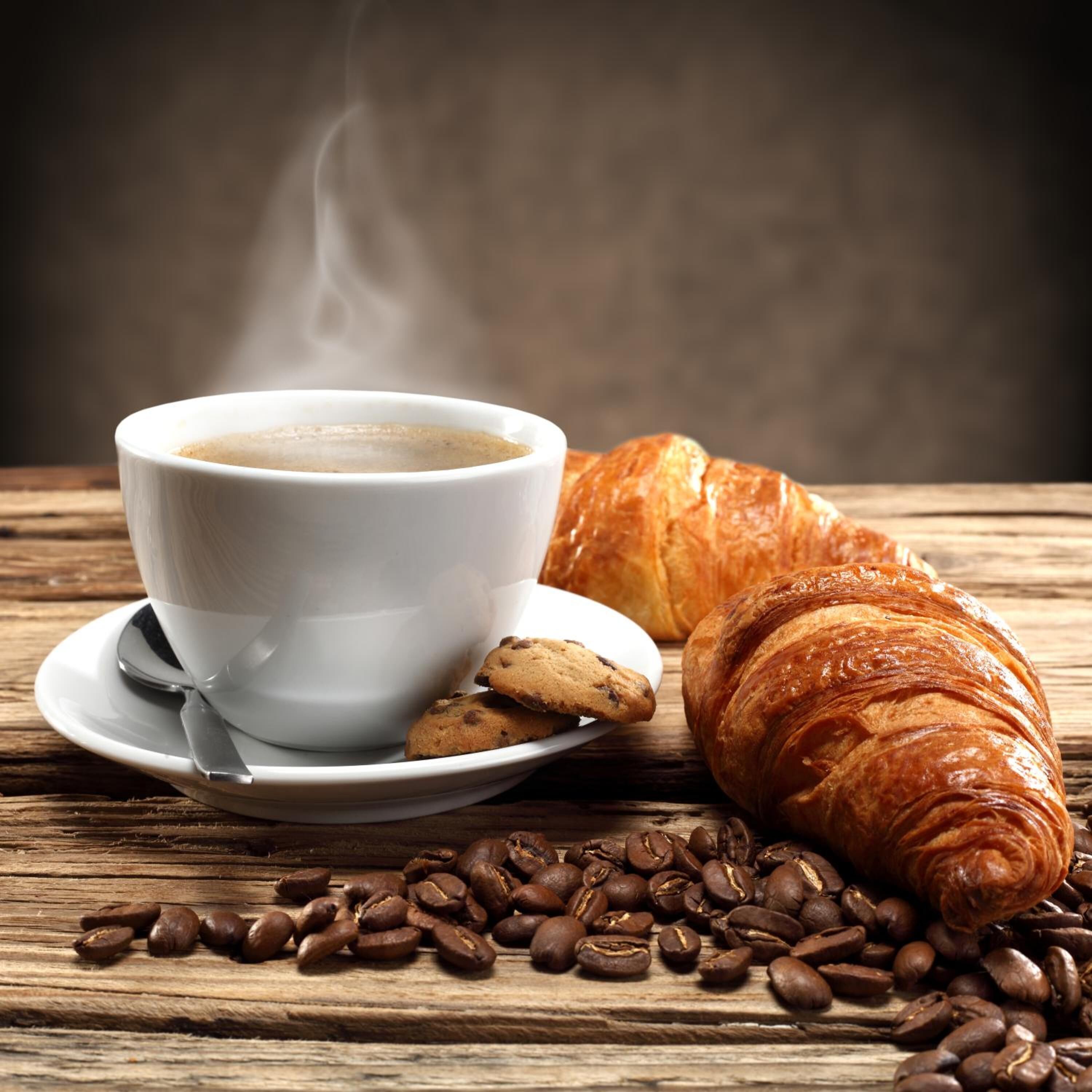 Una taza de café, un croissant y granos de café sobre una superficie de madera.