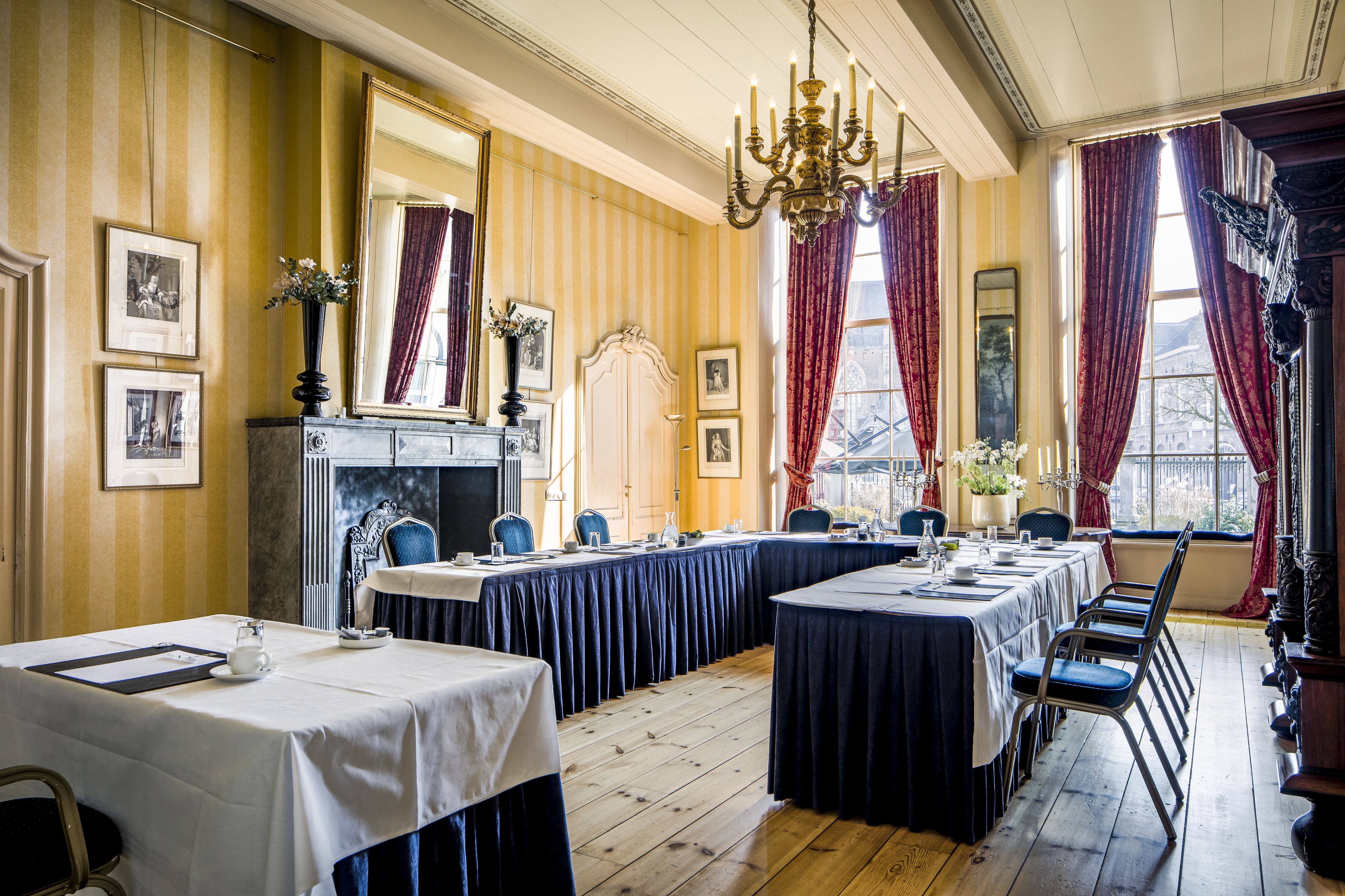 A formal dining room with long tables, chairs, a chandelier, and a fireplace.