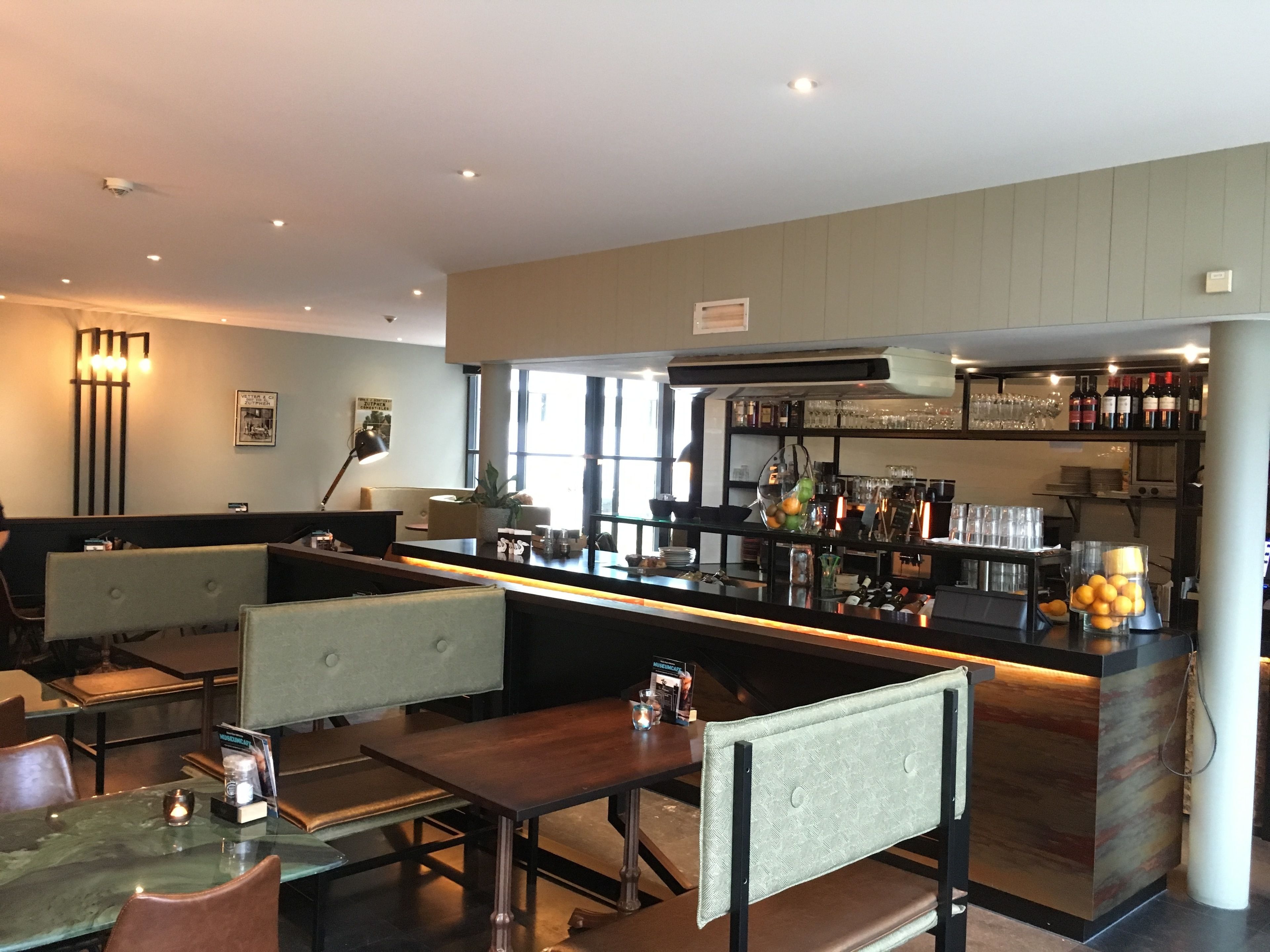 Un restaurante con zona de bar, disposición de mesas y vistas a la calle.
