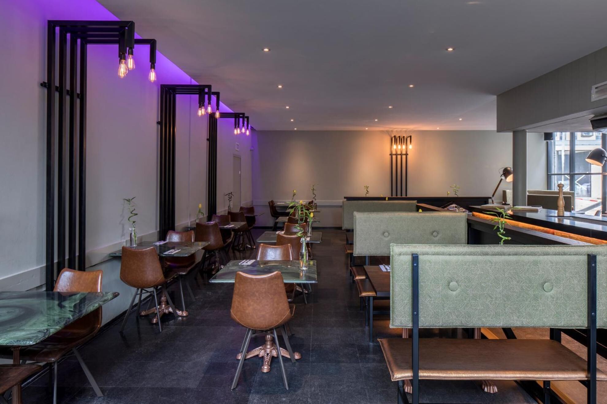 Ein modernes Restaurant-Interieur mit hohen Tischen und Stühlen, gedämpfter Beleuchtung und Blick auf die Stadt durch große Fenster.