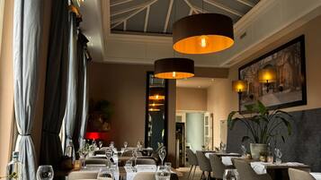 A restaurant with tables set for dining, featuring a high ceiling with a skylight and pendant lighting.