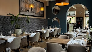 Een restaurant met meerdere eettafels gedekt voor gasten, met een modern interieur, een hoge plafond en hanglampen.