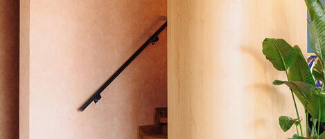 A staircase with wooden steps and a handrail, leading to a landing with a wooden column and a potted plant.