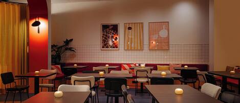 A restaurant with multiple tables and chairs, a red accent wall, and framed artwork on the wall.