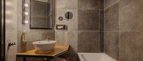 Un baño moderno con una bañera grande, un tocador de madera con un lavabo blanco y un espejo con iluminación.