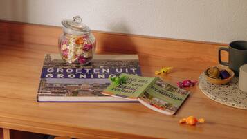 A wooden table with a book titled 'Groeten UIT GRONNING', a glass jar with candies, a coffee mug, and a bowl of chocolates.