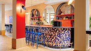 Un área de bar moderna con un llamativo diseño mural abstracto, estanterías rojas y taburetes azules.